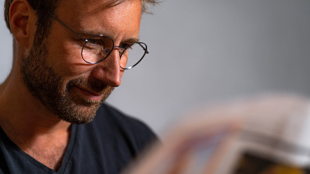 En mand i sort t-shirt læser en avis med Luxreaders læsebriller